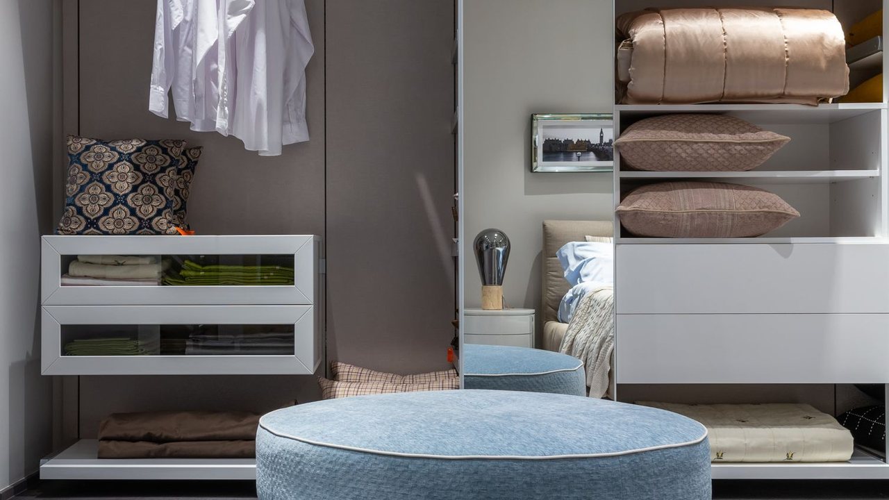Open wardrobe with hanging clothes, shelves and a seat in front
