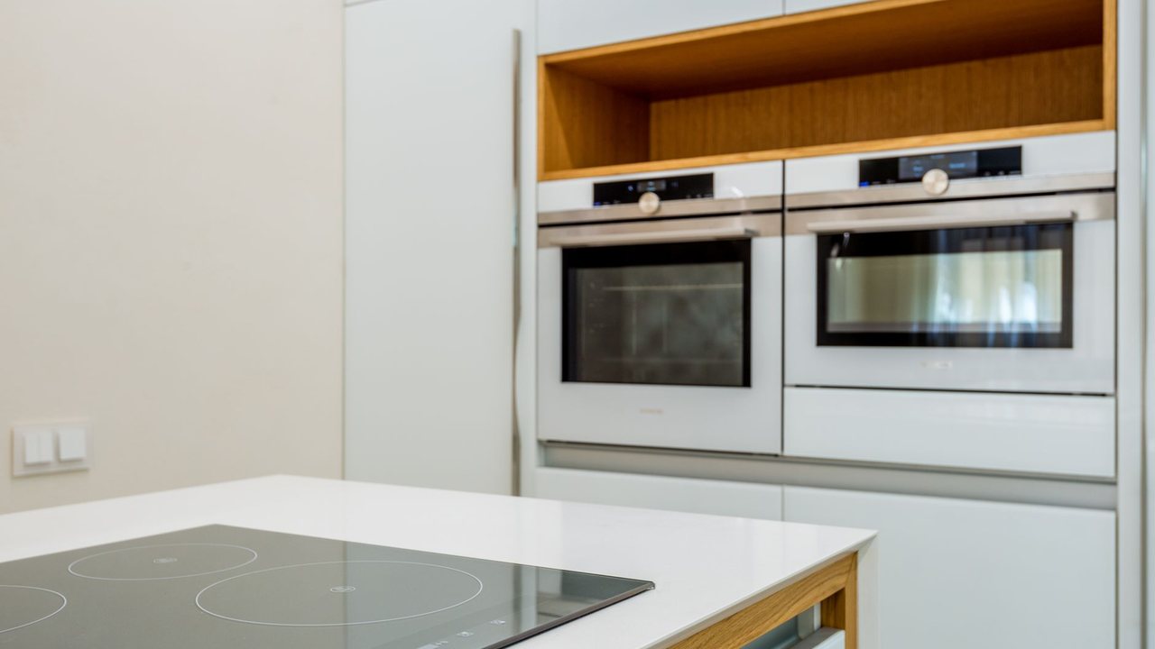 Cocina blanca con placa en la encimera y hornos empotrados