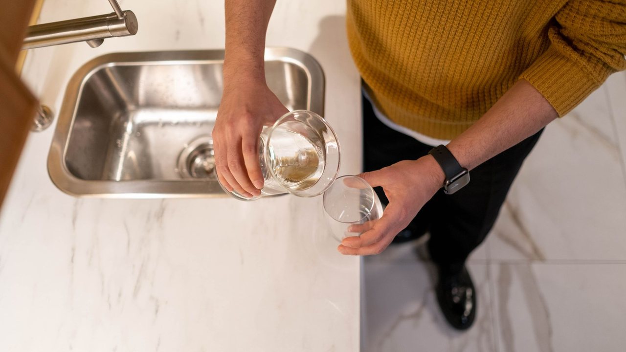 Person pouring water into a glass beside a kitchen sink