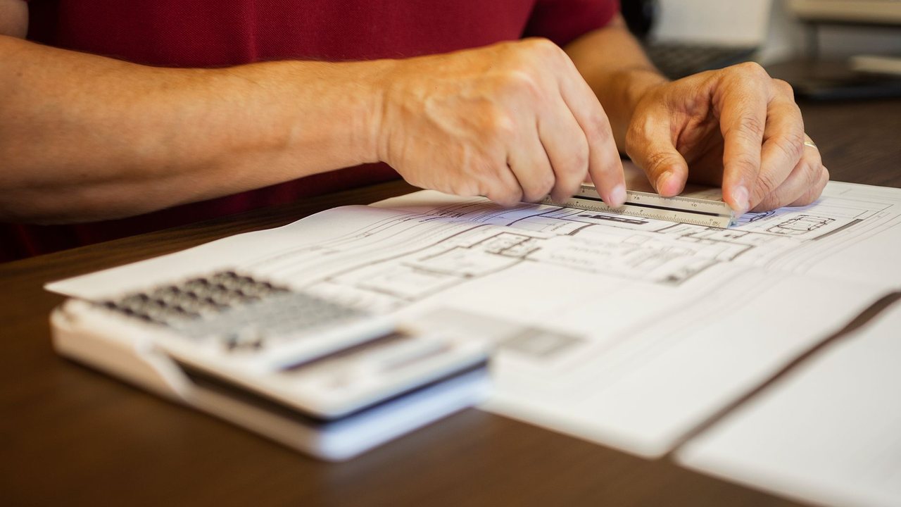 Manos revisando un plano con una regla y una calculadora