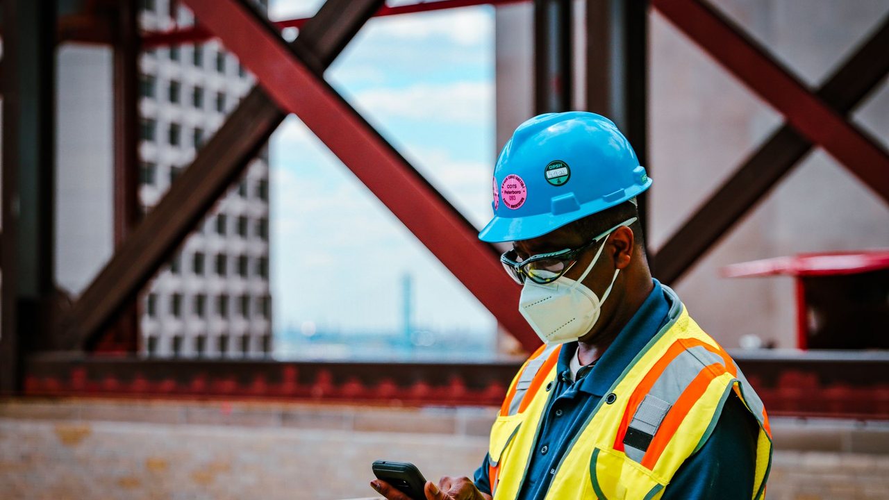 Trabajador con casco y chaleco consultando un teléfono en una obra