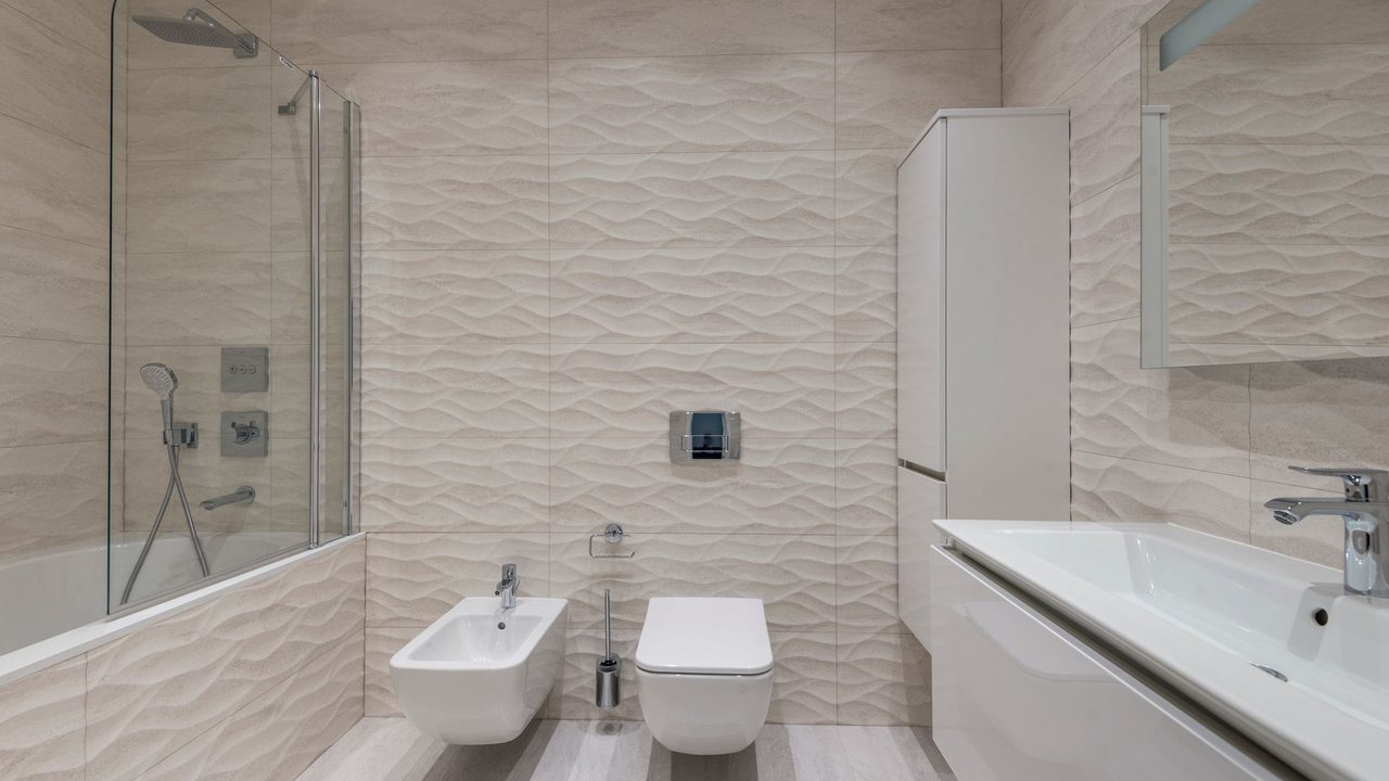 Inodoro y bidé suspendidos frente a una pared de azulejos con relieve