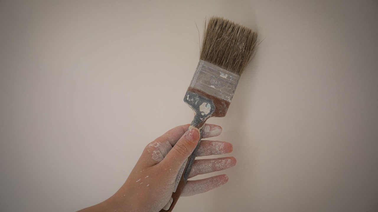 Hand holding a paintbrush in front of a light-coloured wall