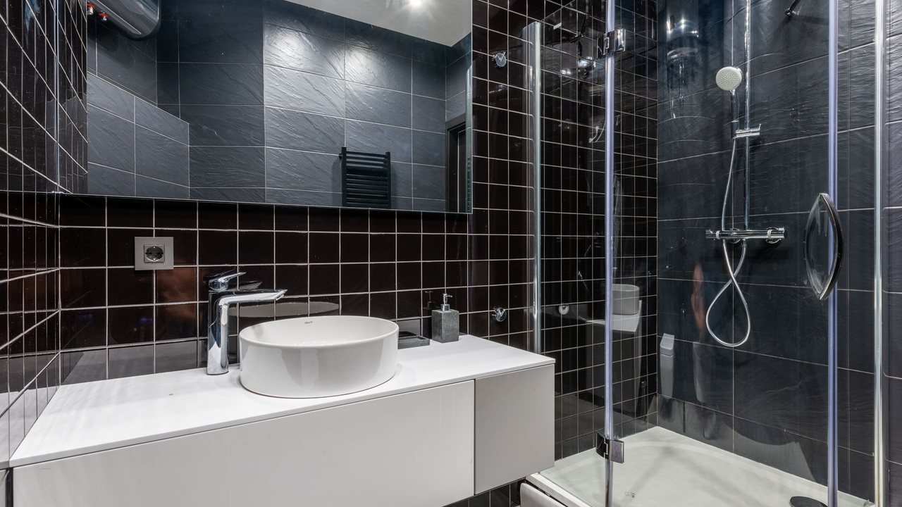 Baño con baldosas oscuras, juntas claras y ducha acristalada